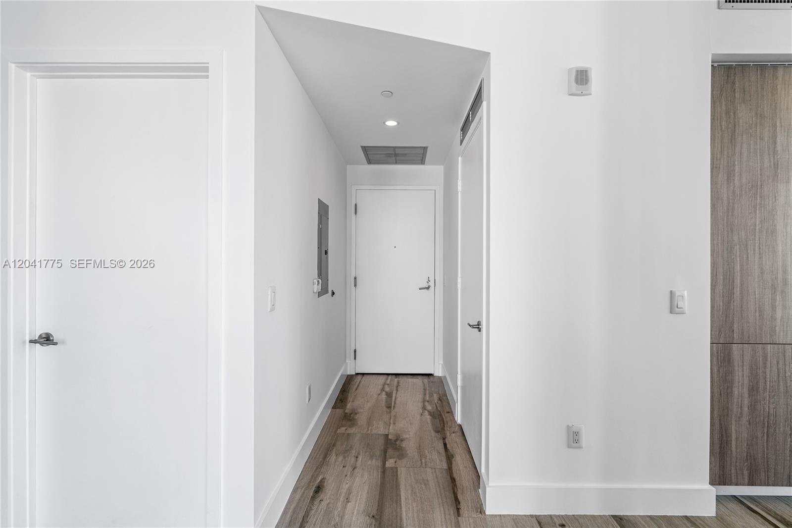 A hallway with white walls, wood-look flooring, and several closed doors leads to an entrance — 2900 NE 7th Ave # 1609, Miami FL 33137, MIAMI, FL