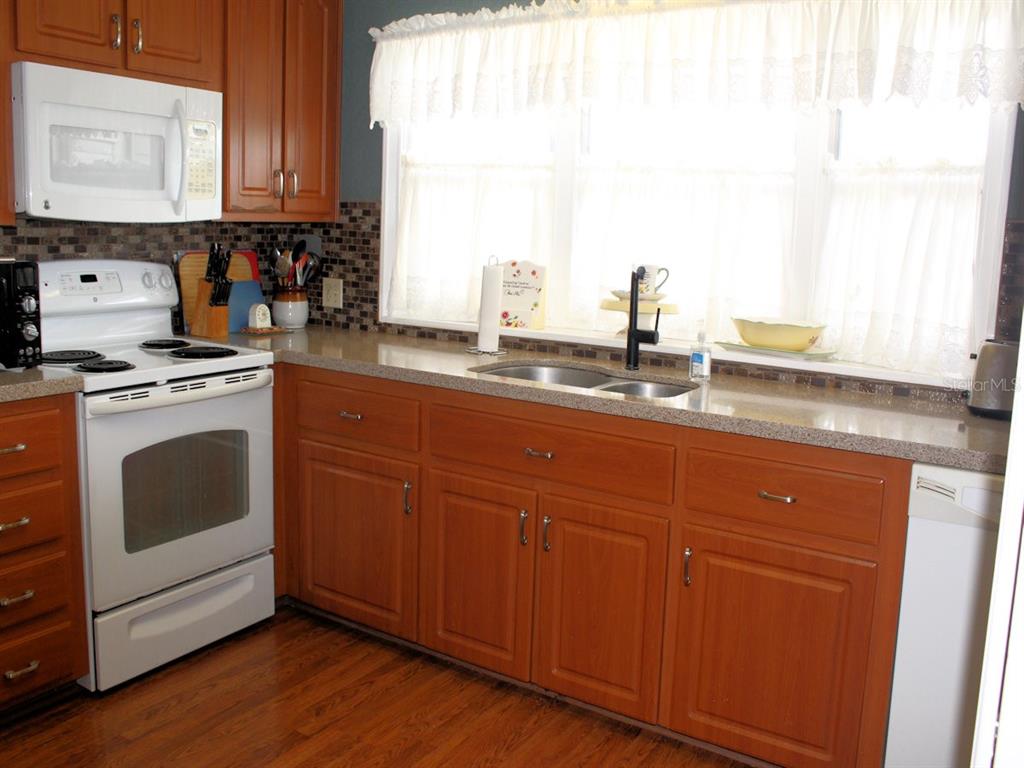 A kitchen with wood cabinets, a white stove, a microwave, and a window above the sink — 26 ROYAL PALM CIRCLE, LARGO, FL