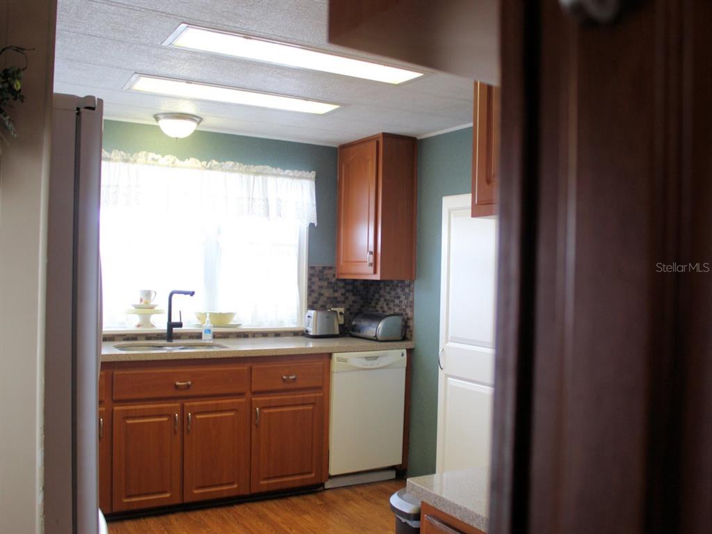 A kitchen features wood cabinets, a white dishwasher, a window, and a tiled backsplash — 26 ROYAL PALM CIRCLE, LARGO, FL