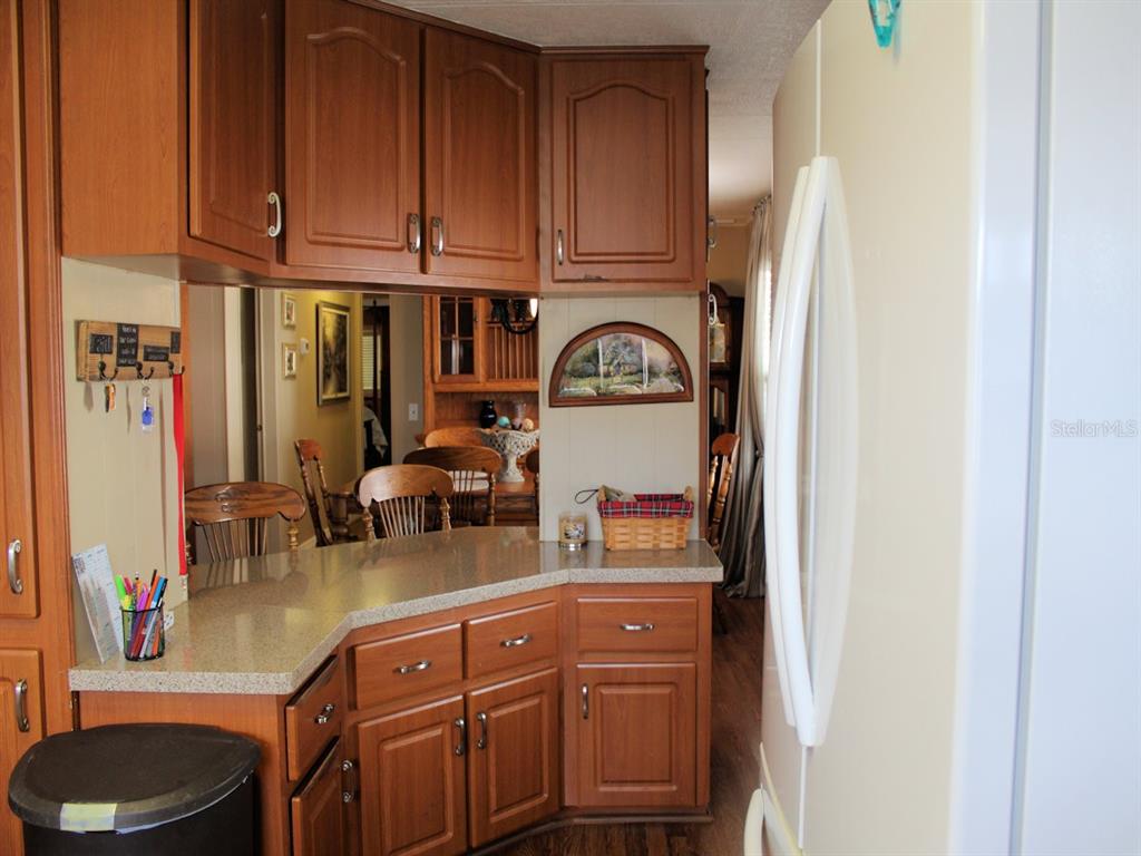 A kitchen features wood cabinets, a laminate countertop, and a view into the dining area — 26 ROYAL PALM CIRCLE, LARGO, FL