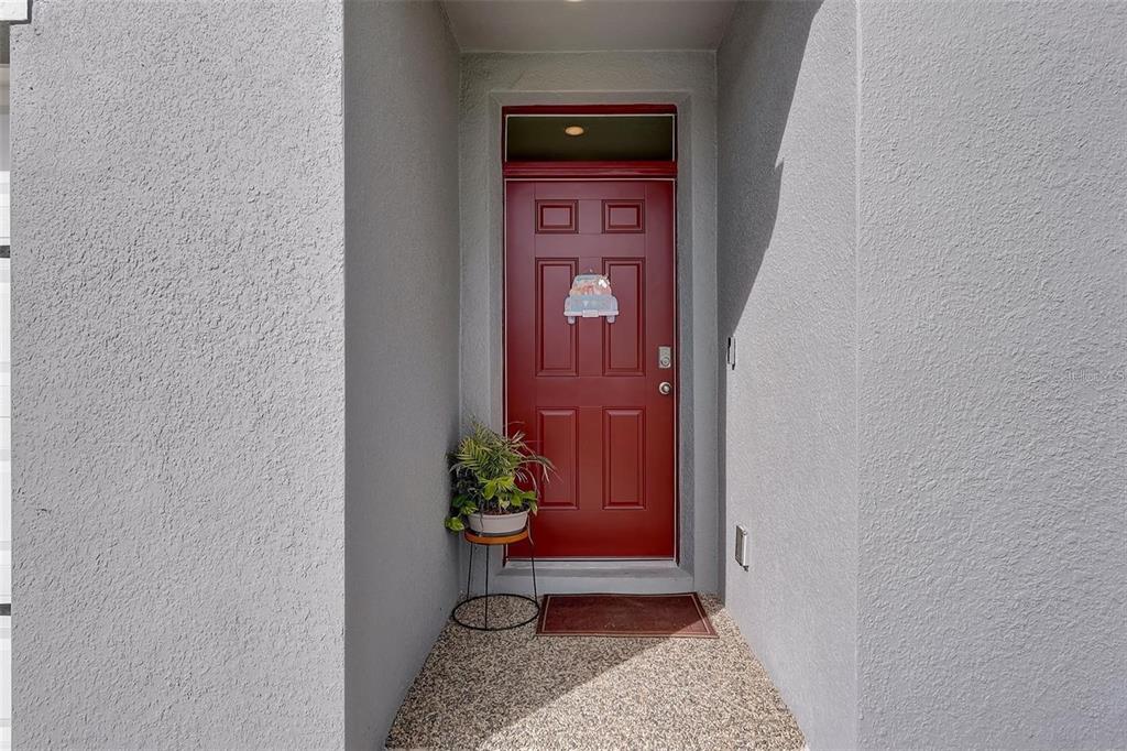 A red front door is set within a recessed entryway with gray stucco walls — 2076 TAY WES DR, ST CLOUD, FL