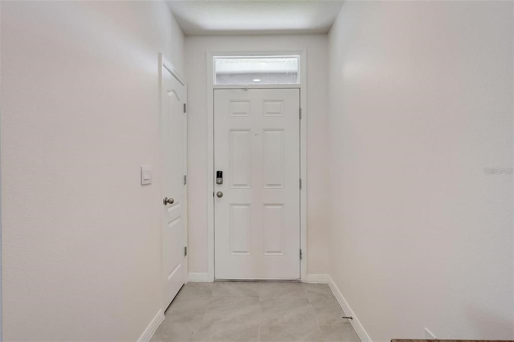 A white front door with a transom window sits at the end of a tiled entryway — 2076 TAY WES DR, ST CLOUD, FL