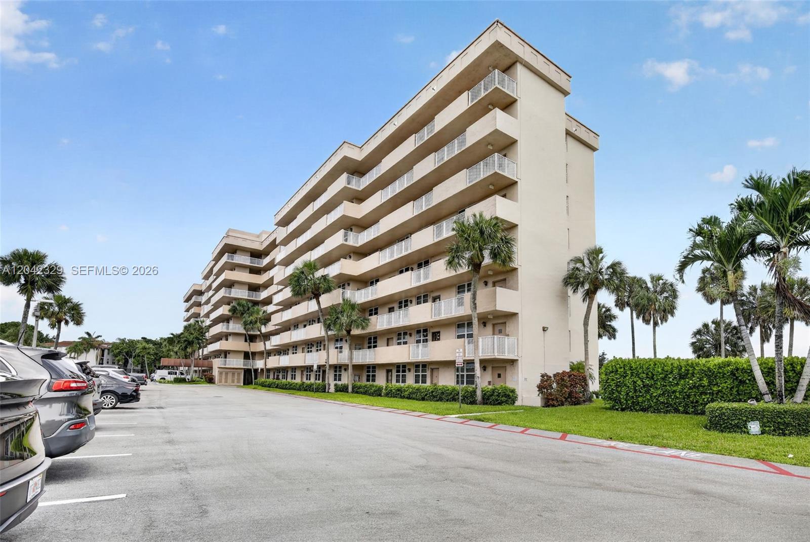 A multi-story apartment building stands next to a parking lot with several parked cars — 250 Jacaranda Dr # 411, Plantation FL 33324, PLANTATION, FL
