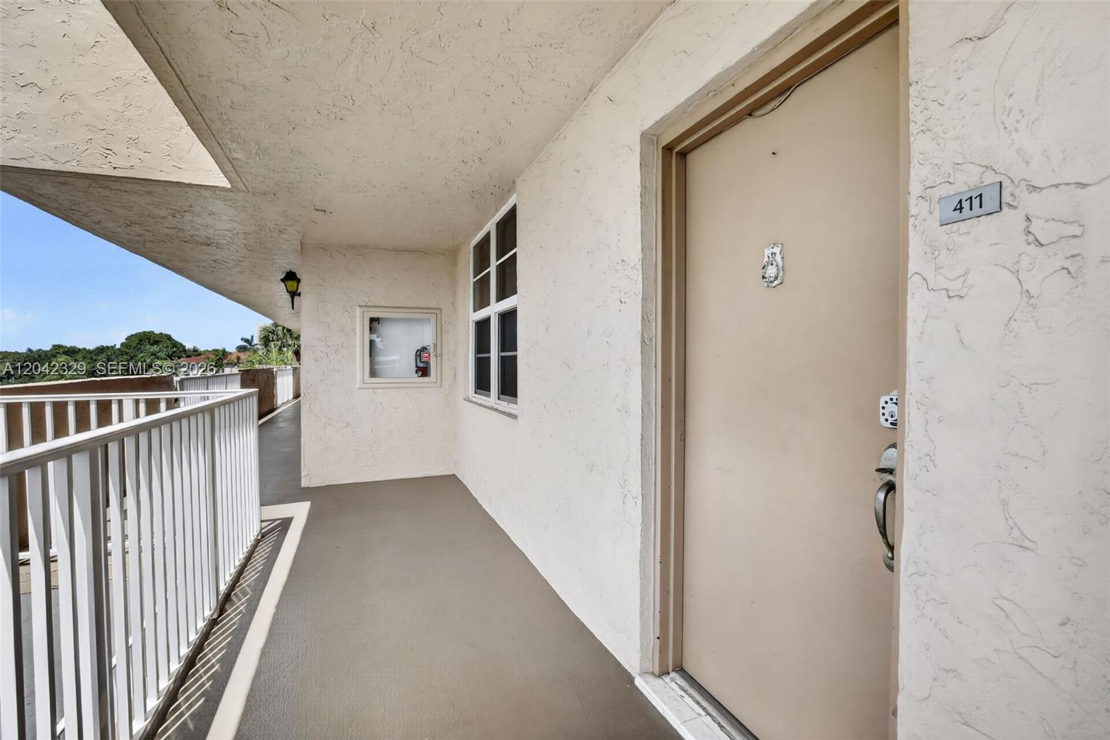 An exterior hallway features a beige door labeled 411, a white railing, and a window — 250 Jacaranda Dr # 411, Plantation FL 33324, PLANTATION, FL