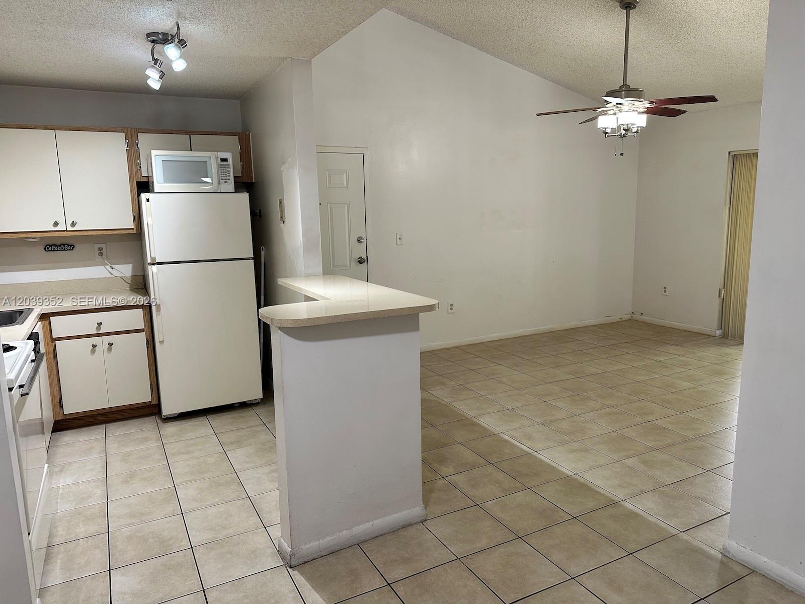 A kitchen with white appliances and cabinets opens into a tiled living area with vaulted ceilings — 7200 NW 179th St # 311, Hialeah FL 33015, HIALEAH, FL