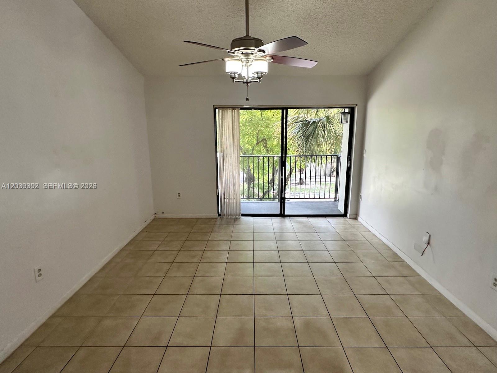 An empty room features beige tile flooring, a ceiling fan, and a sliding glass door — 7200 NW 179th St # 311, Hialeah FL 33015, HIALEAH, FL