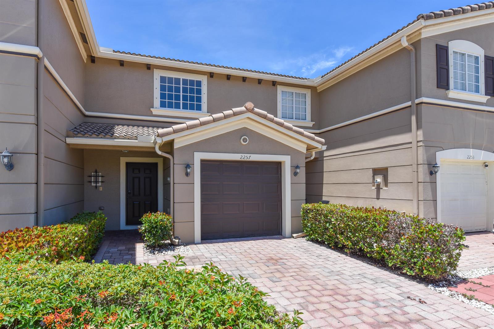The exterior of a two-story townhouse features a brown garage, a front door, and landscaping — 2257 SW Marshfield Court, FL 34953, FL