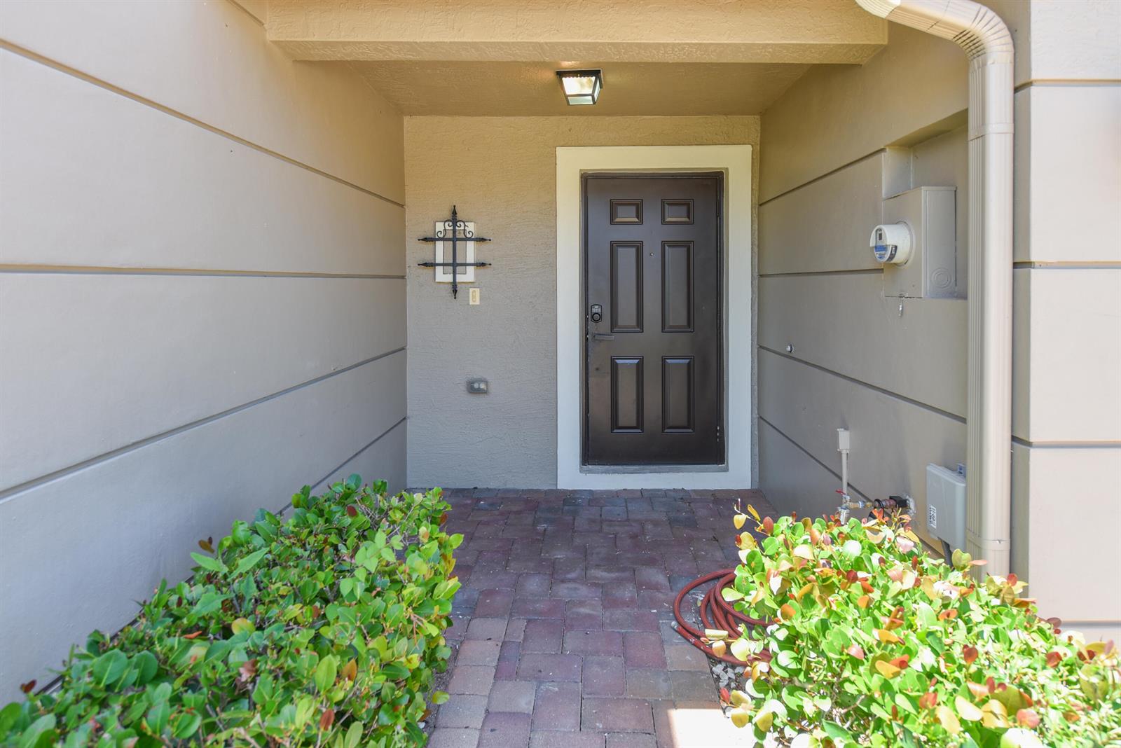 A brown front door is centered in a recessed entryway with paved flooring and landscaping — 2257 SW Marshfield Court, FL 34953, FL