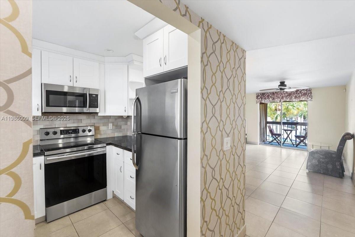 A kitchen with stainless steel appliances and white cabinets opens to a living area — 2755 W Atlantic Ave # 2208, Delray Beach FL 33445, DELRAY BEACH, FL