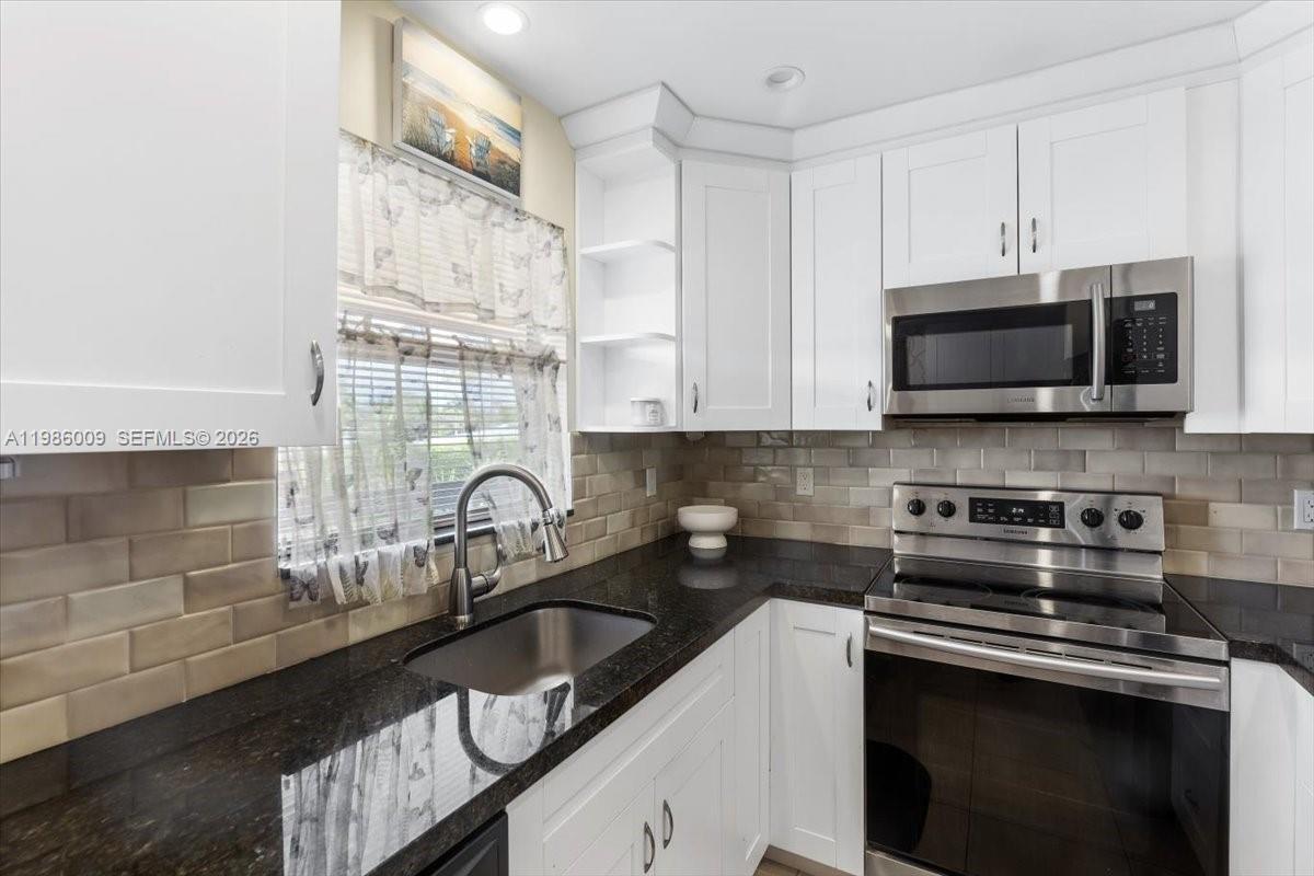 A kitchen features white cabinets, dark granite countertops, stainless steel appliances, and a subway tile backsplash — 2755 W Atlantic Ave # 2208, Delray Beach FL 33445, DELRAY BEACH, FL