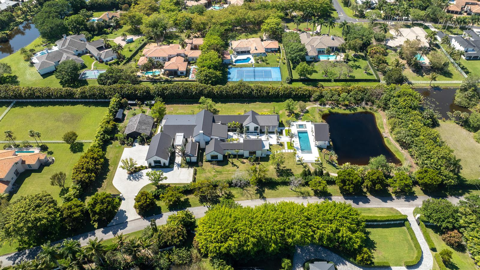 An aerial view shows a large modern house with a pool and pond on a lot — 10468 El Caballo Court, Delray Beach FL 33446, DELRAY BEACH, FL