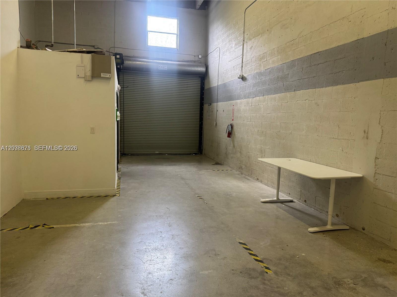 An industrial warehouse space features a concrete floor, a roll-up door, and a white table — 10171 NW 58th St # 6, Doral FL 33178, DORAL, FL