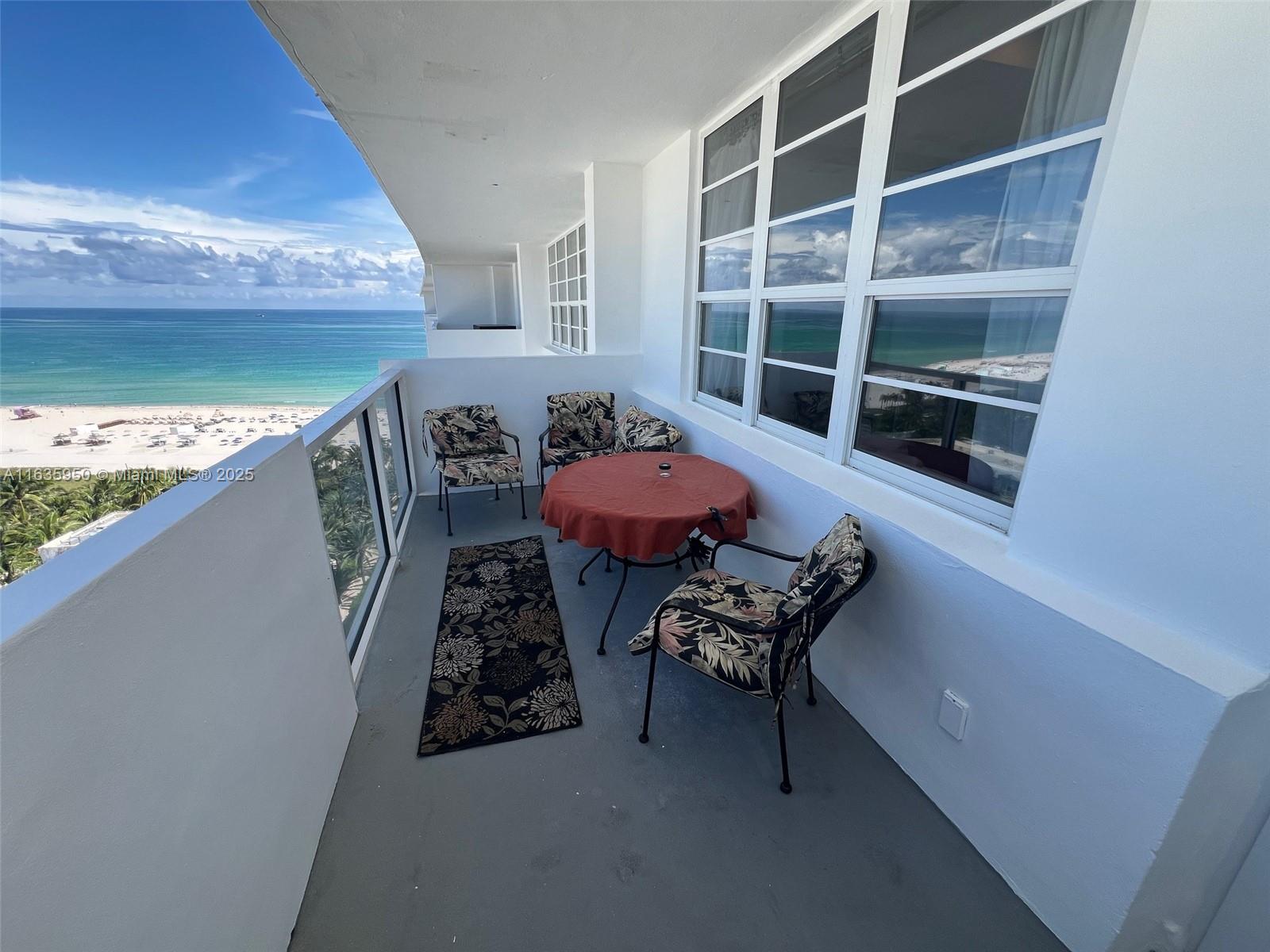 A balcony with a table, chairs, and a rug overlooks the ocean and beach — 100 Lincoln Rd # 1633, Miami Beach FL 33139, MIAMI BEACH, FL
