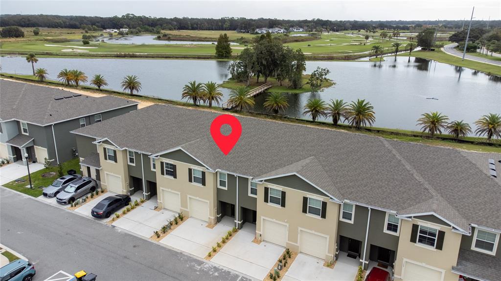 An aerial view shows a row of townhouses with attached garages and a nearby lake — 1153 BLUE JAY DRIVE, DAVENPORT, FL