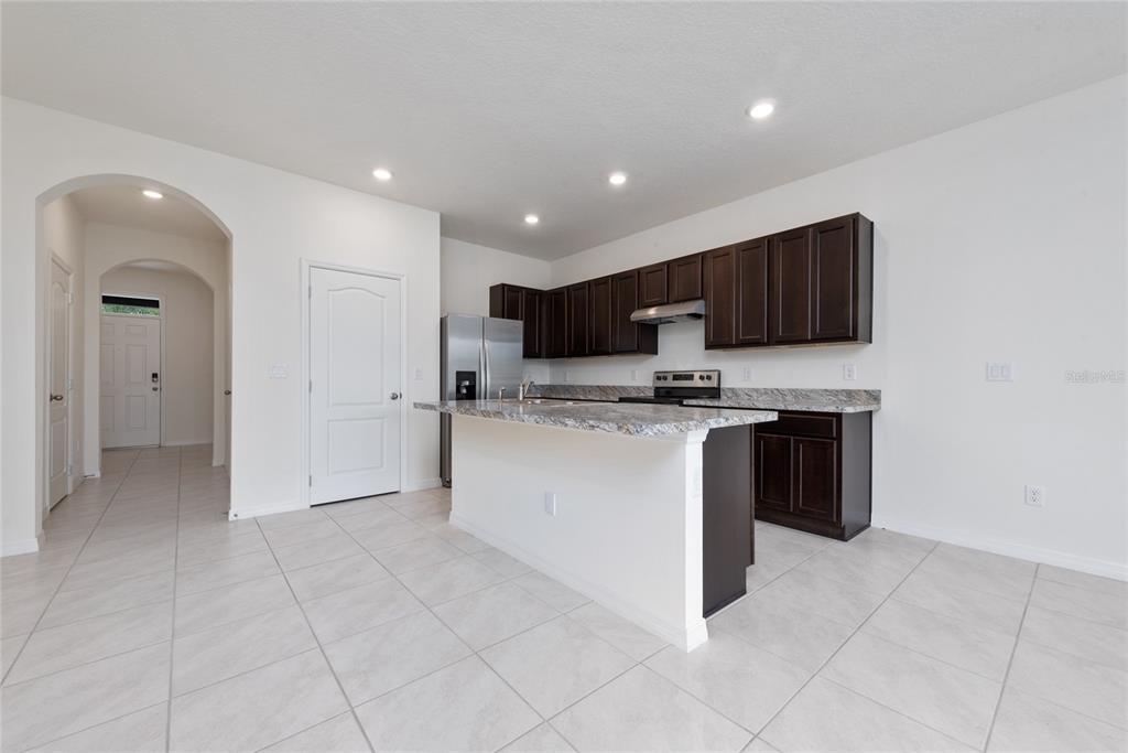 A kitchen with dark wood cabinets, granite countertops, a center island, and light tile flooring — 1153 BLUE JAY DRIVE, DAVENPORT, FL