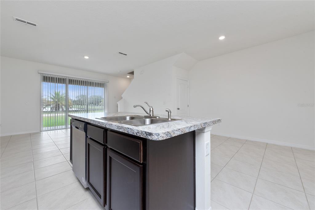A kitchen island with a granite countertop and dark cabinets sits in a tiled room — 1153 BLUE JAY DRIVE, DAVENPORT, FL