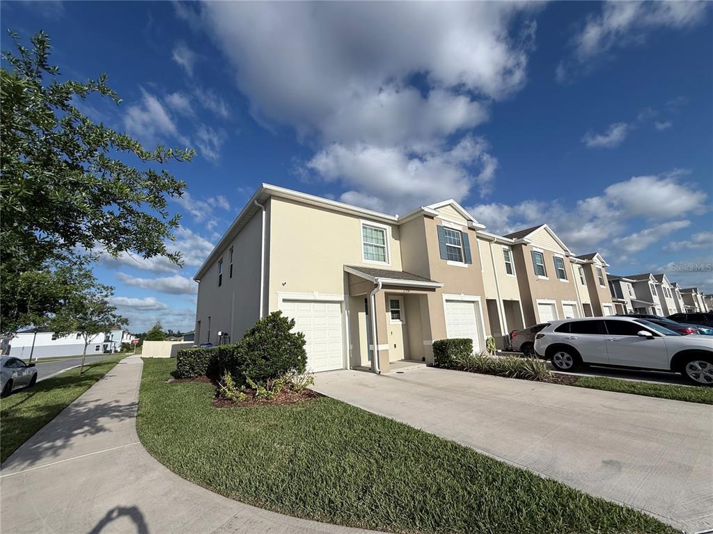 A two-story townhouse with a beige stucco exterior, a concrete driveway, and a small lawn — 2354 TAY WES DRIVE, ST CLOUD, FL
