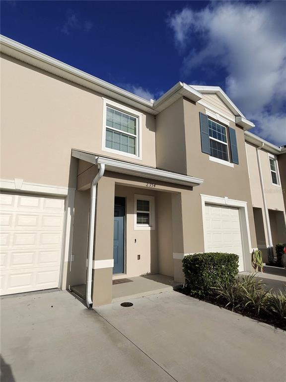A two-story townhouse exterior features a beige facade, a garage, and a covered entryway — 2354 TAY WES DRIVE, ST CLOUD, FL