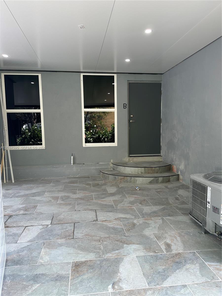 A covered patio features gray stone tile flooring, two windows, and a small set of steps — 1628 NW 15th St # B, Miami FL 33125, MIAMI, FL