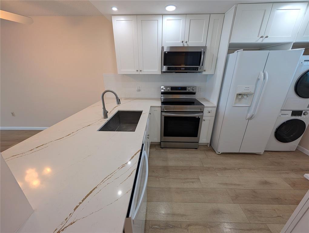 A kitchen features white cabinets, stainless steel appliances, and a white countertop with gold veining — 18304 GULF BOULEVARD UNIT 406, REDINGTON SHORES, FL