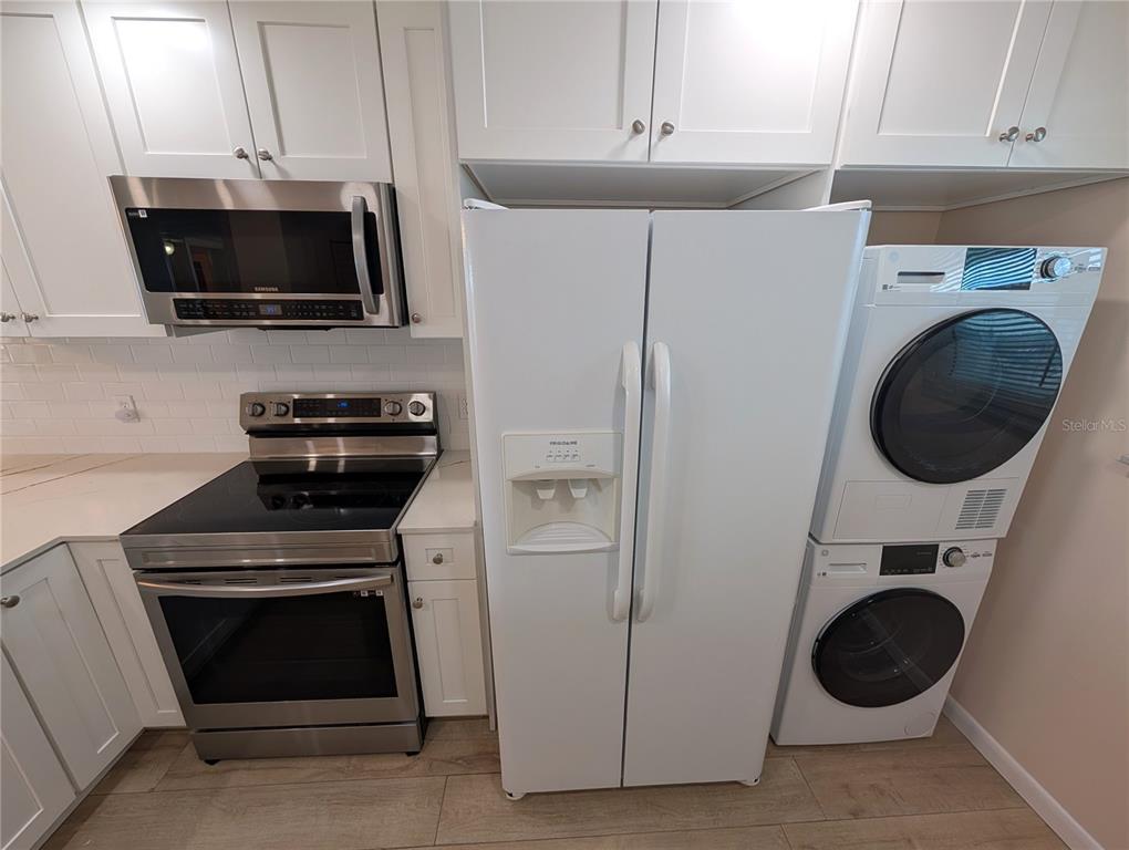 A kitchen features white cabinets, stainless steel appliances, a refrigerator, and a stacked laundry unit — 18304 GULF BOULEVARD UNIT 406, REDINGTON SHORES, FL