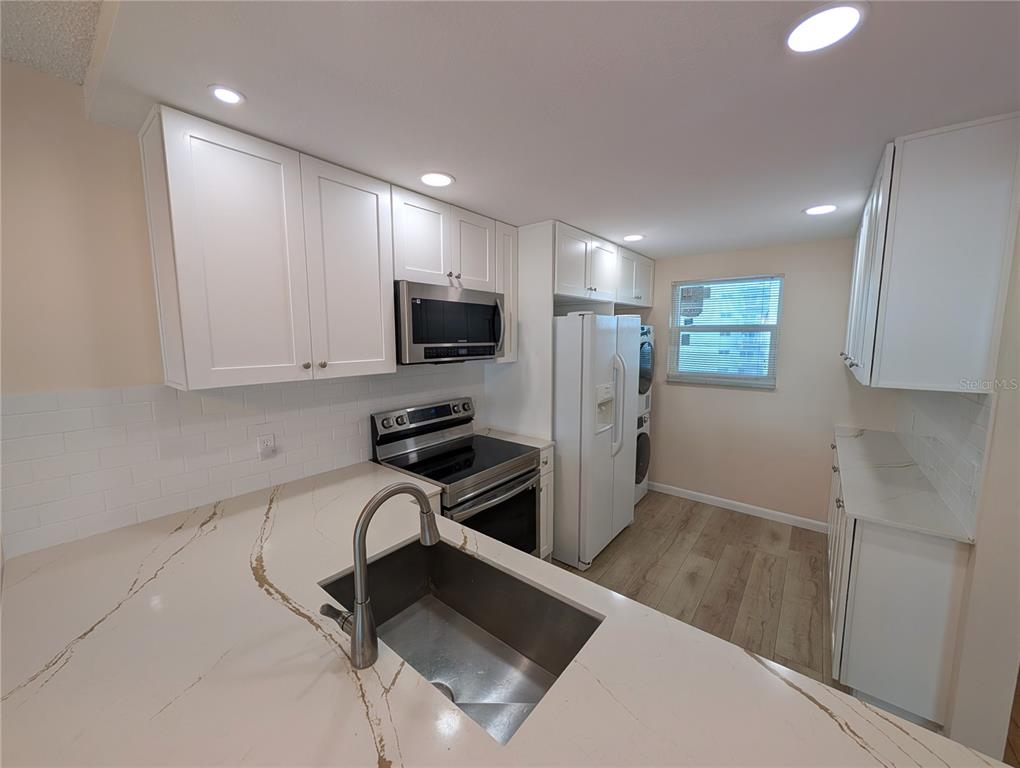 A kitchen features white cabinets, stainless steel appliances, a sink, and light-colored stone countertops — 18304 GULF BOULEVARD UNIT 406, REDINGTON SHORES, FL