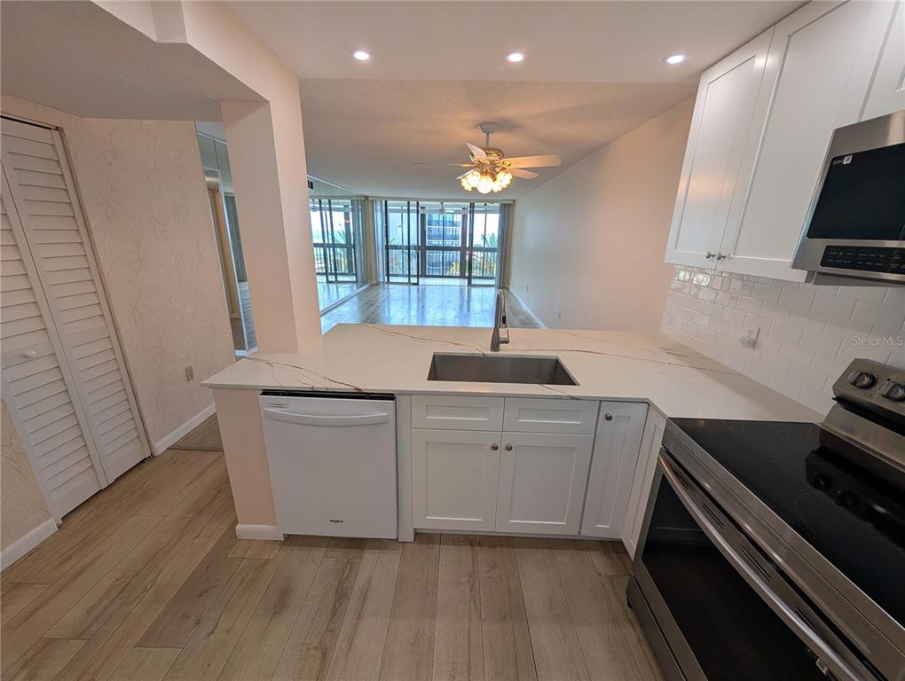 A kitchen features white cabinets, a marble-look countertop, stainless steel appliances, and wood-look flooring — 18304 GULF BOULEVARD UNIT 406, REDINGTON SHORES, FL