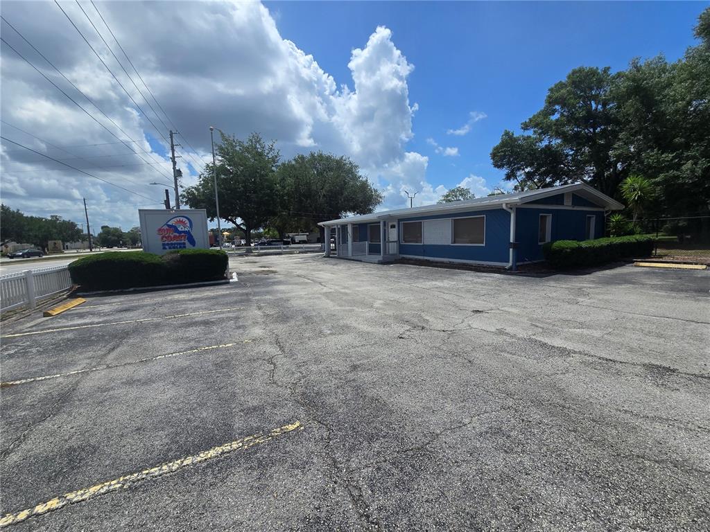 A blue commercial building sits on a large, cracked asphalt parking lot under a cloudy sky — 531 DOG TRACK ROAD, LONGWOOD, FL