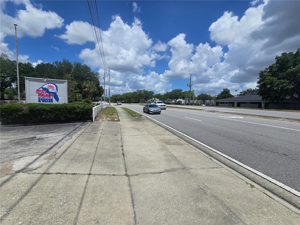 A sidewalk runs alongside a multi-lane road with a Sun Coast Roofing sign nearby — 531 DOG TRACK ROAD, LONGWOOD, FL