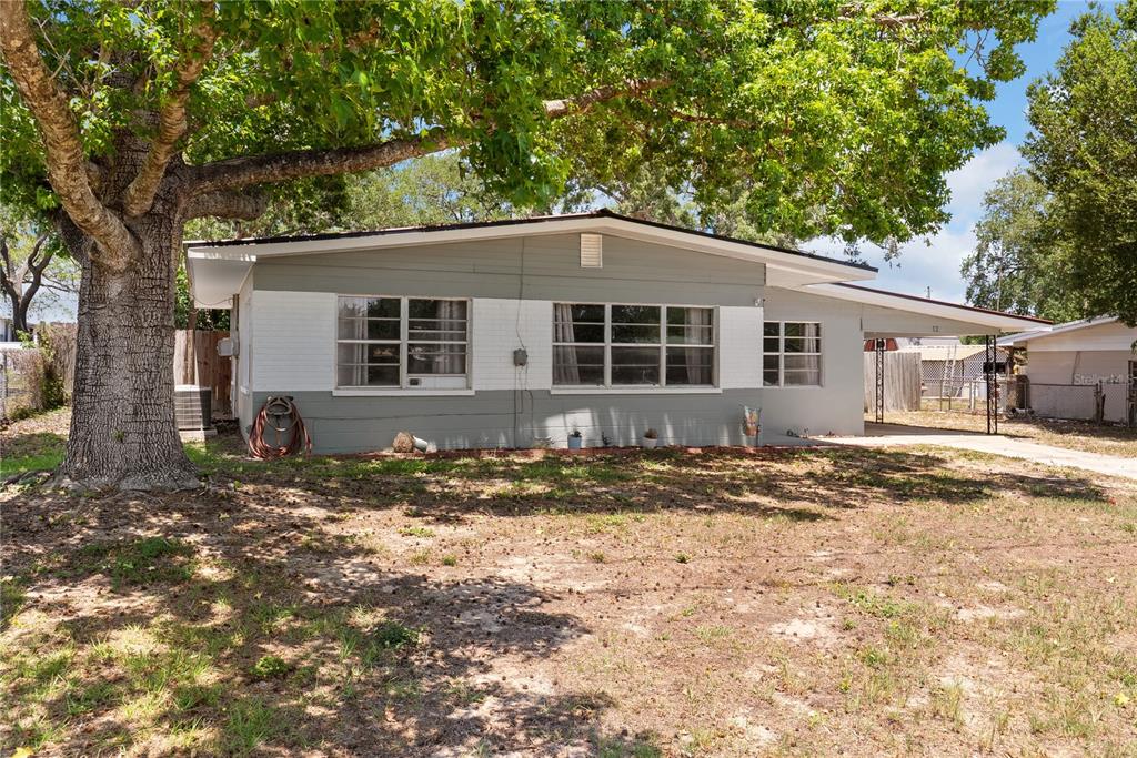 A single-story house with a gray and white exterior sits behind a large tree — 12 BEVERLY DRIVE, FROSTPROOF, FL