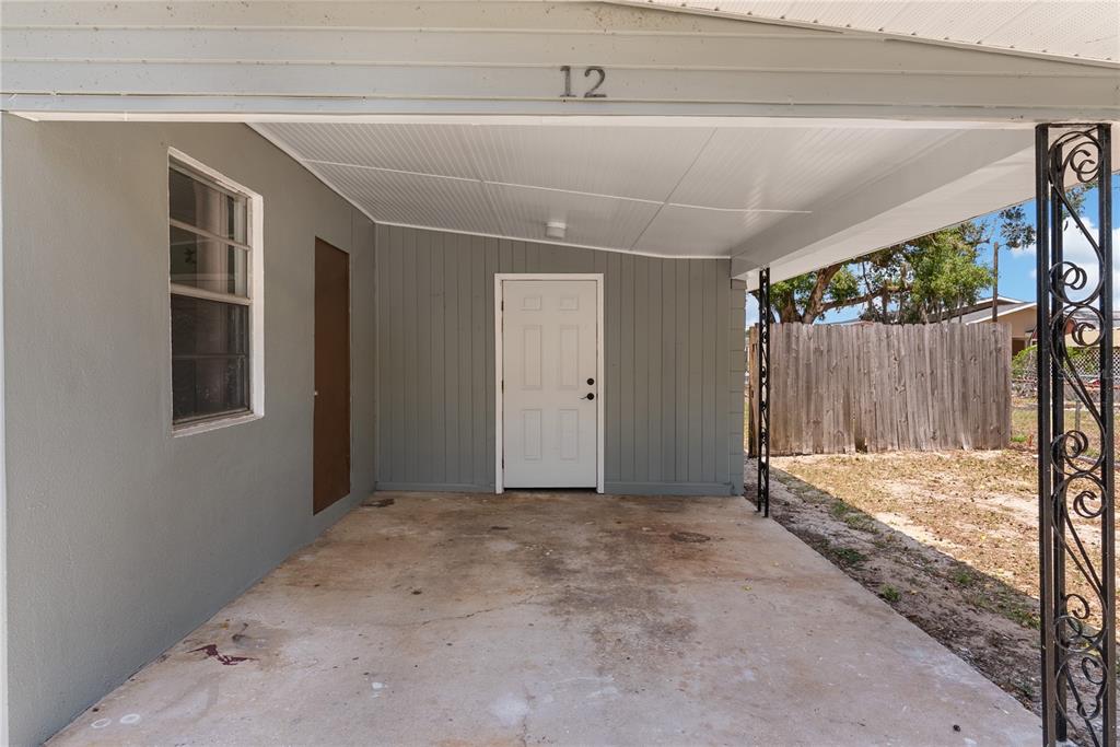 A covered concrete carport features a white door, a window, and decorative metal support columns — 12 BEVERLY DRIVE, FROSTPROOF, FL