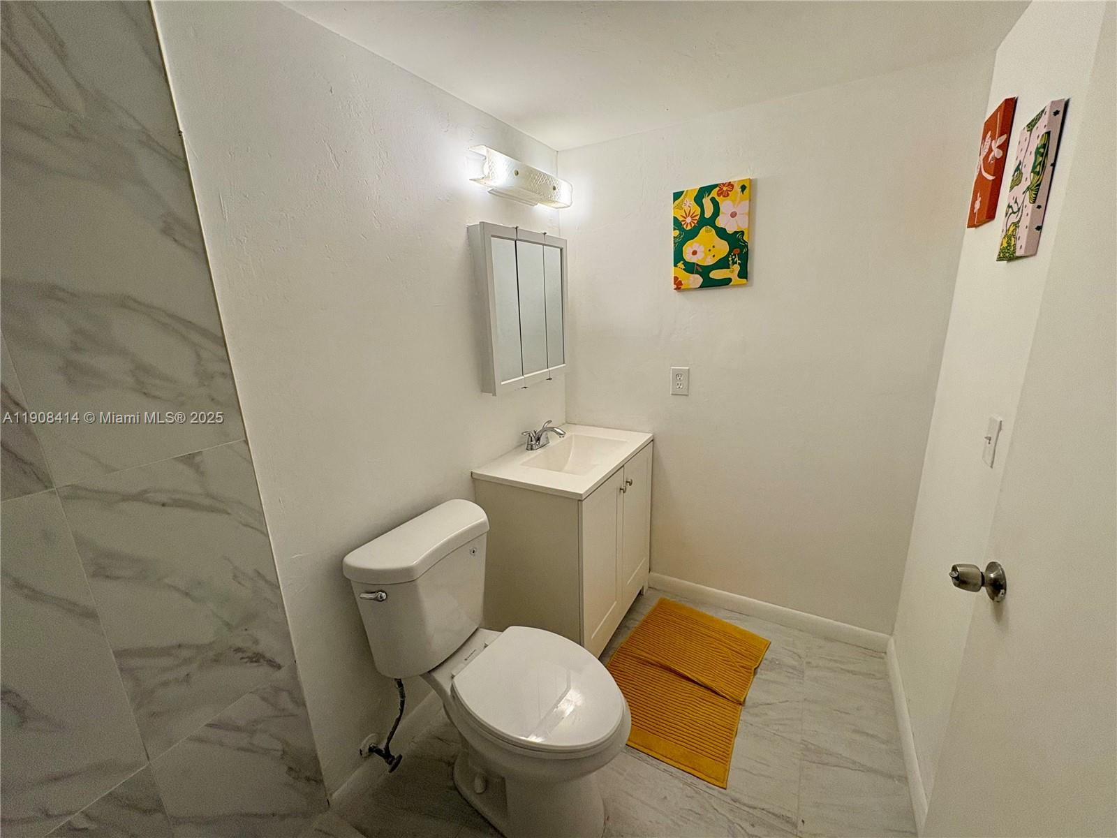 A bathroom features a white vanity, a toilet, and marble-look tile flooring and walls — 7310 NW 1st St # 105, Margate FL 33063, MARGATE, FL