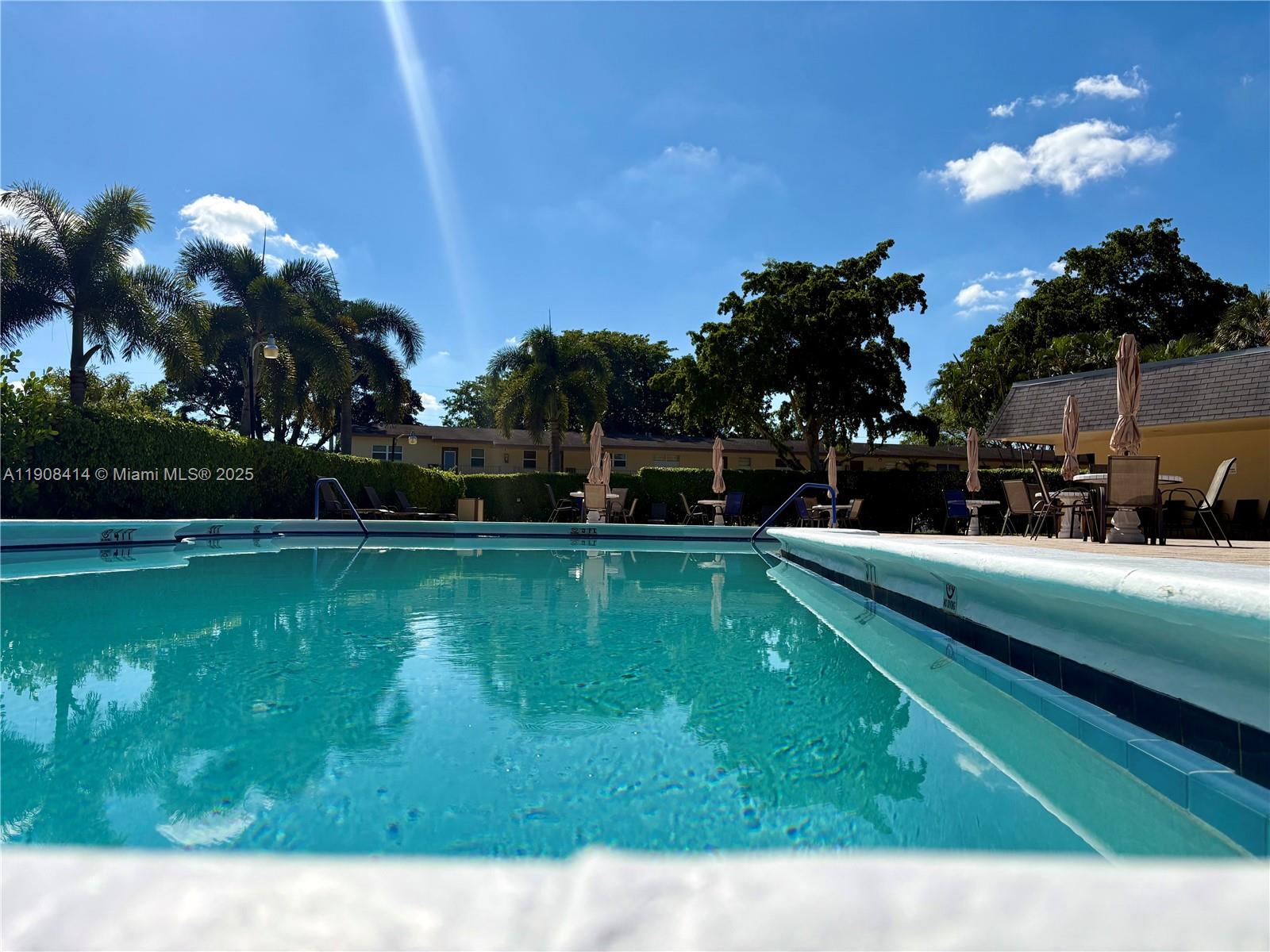 A swimming pool with lounge chairs and umbrellas on the deck under a blue sky — 7310 NW 1st St # 105, Margate FL 33063, MARGATE, FL