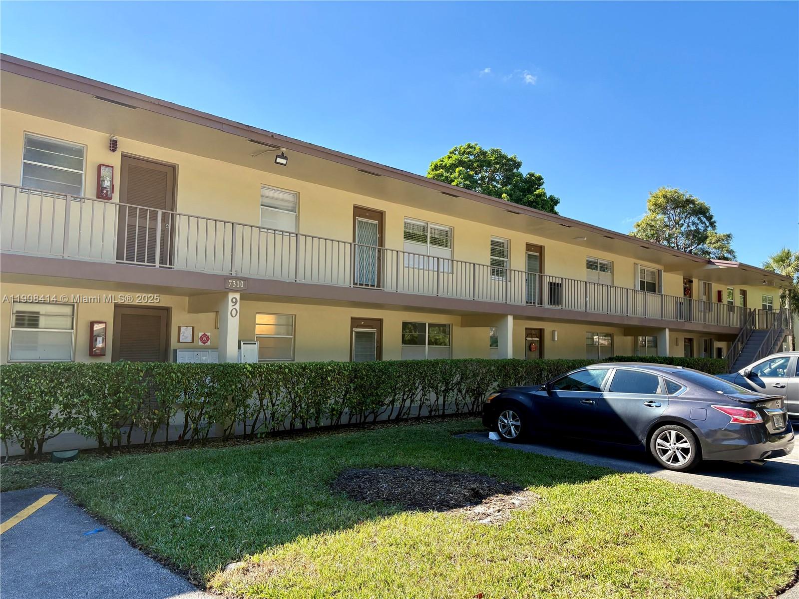 A two-story apartment building features a long exterior walkway with metal railings and landscaping — 7310 NW 1st St # 105, Margate FL 33063, MARGATE, FL