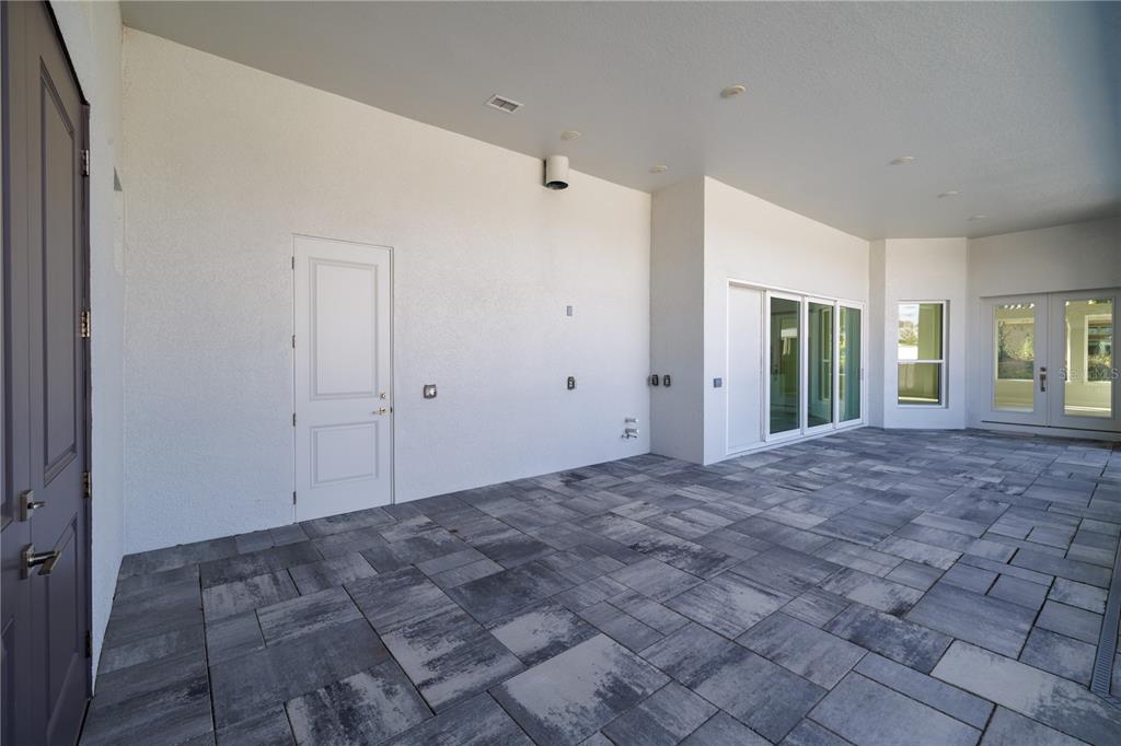 A covered patio with gray paver flooring, white walls, and multiple glass entry doors — 110 NEW LEATHERWOOD DRIVE, PALM COAST, FL