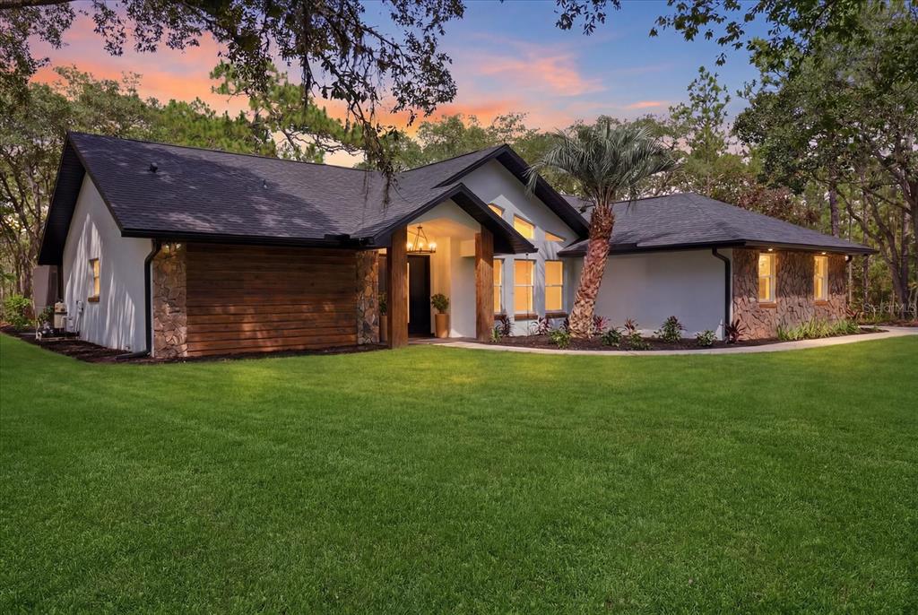 A modern single-story house with white stucco, stone accents, and wood siding at sunset — 2995 N BRAVO DRIVE, BEVERLY HILLS, FL