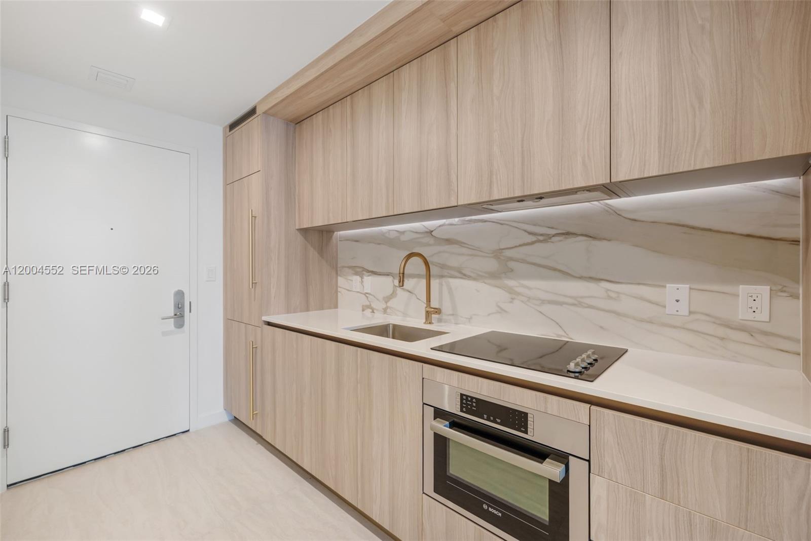 A modern kitchen features light wood cabinets, a marble backsplash, and stainless steel appliances — 77 SE 5th St # 3205, Miami FL 33131, MIAMI, FL