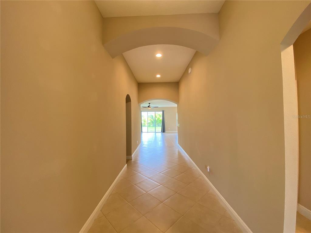 A long hallway with arched ceilings and beige tile flooring leads to a bright living area — 6507 PARK TERRACE LANE, APOLLO BEACH, FL