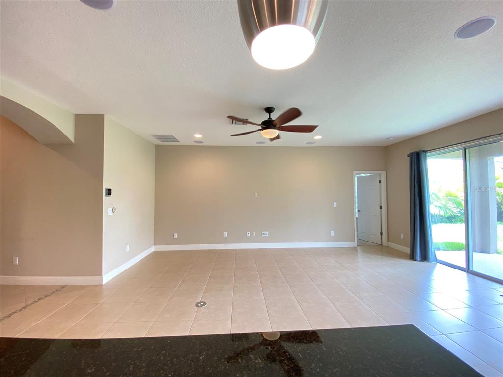 An empty living room features beige walls, tile flooring, a ceiling fan, and sliding glass doors — 6507 PARK TERRACE LANE, APOLLO BEACH, FL