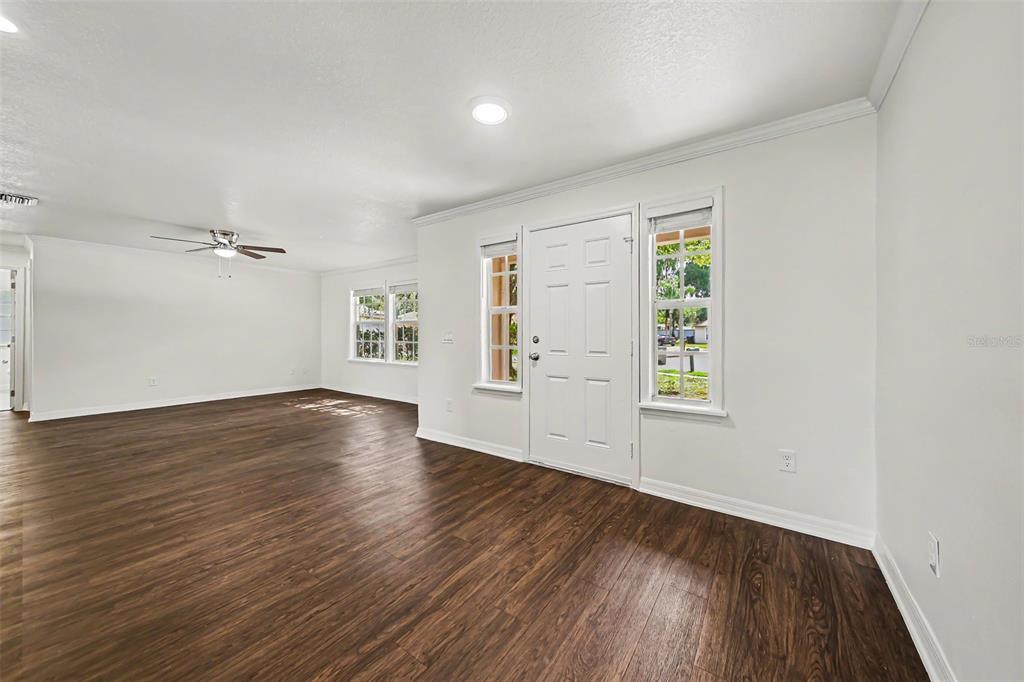 An empty living room with white walls, dark wood-look flooring, and a white front door — 245 OAK RUN COURT, APOPKA, FL