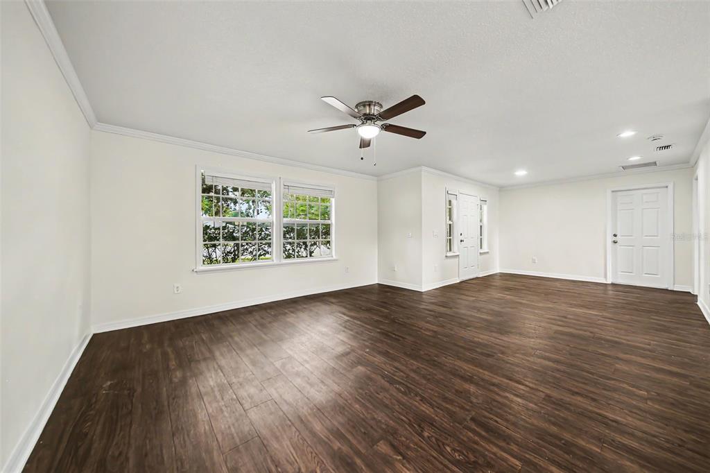 An empty living room features dark wood-look flooring, white walls, and a ceiling fan — 245 OAK RUN COURT, APOPKA, FL