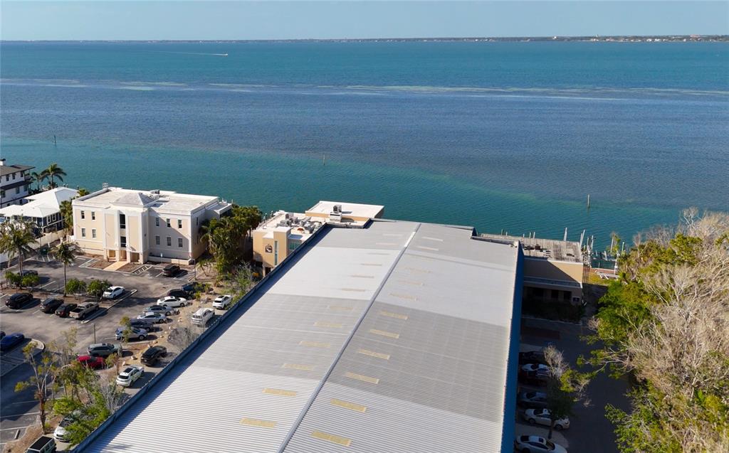 An aerial view shows a large metal-roofed building next to a parking lot and water — 408 GULF OF MEXICO DRIVE UNIT 1214, LONGBOAT KEY, FL