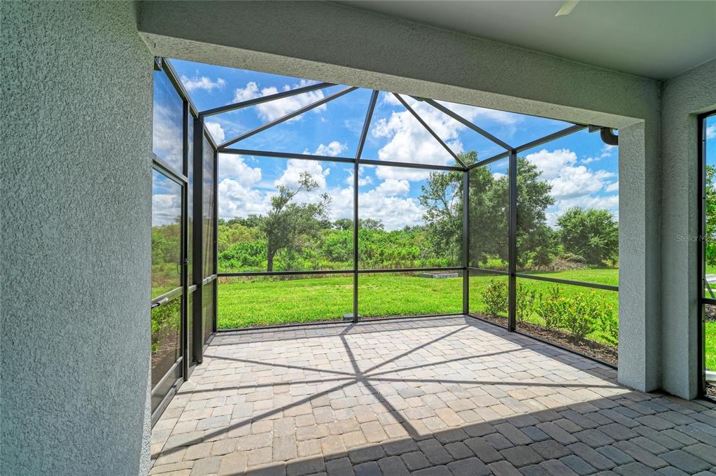 A screened-in patio with paver flooring overlooks a grassy backyard and a line of trees — 18808 INDIAN ROCK PLACE, LAKEWOOD RANCH, FL
