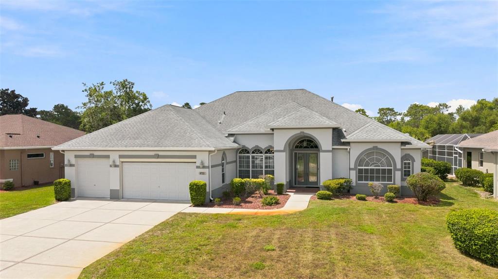 A single-story house with a gray roof, white stucco exterior, and a three-car garage — 8722 MISSISSIPPI RUN, WEEKI WACHEE, FL