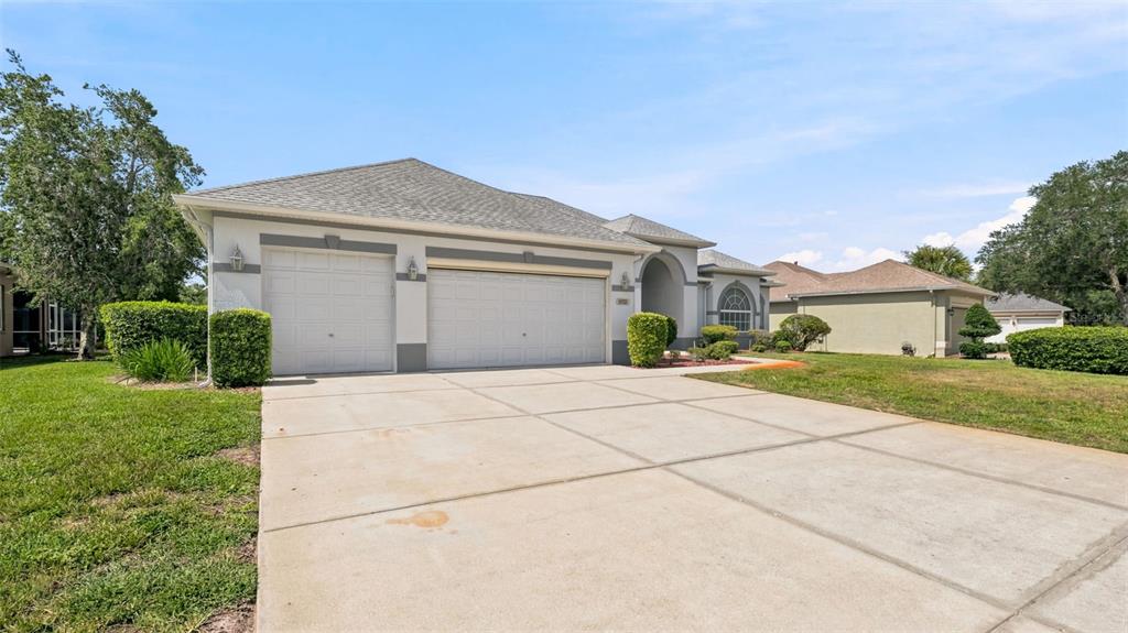 A single-story house with a three-car garage and a concrete driveway under a blue sky — 8722 MISSISSIPPI RUN, WEEKI WACHEE, FL