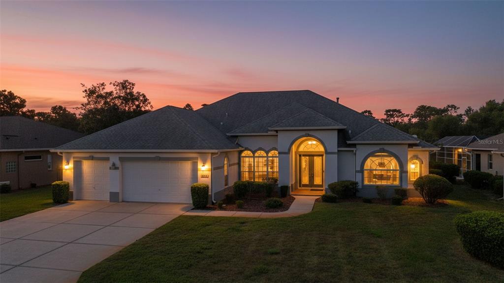 A single-story house with a two-car garage and arched windows at sunset — 8722 MISSISSIPPI RUN, WEEKI WACHEE, FL