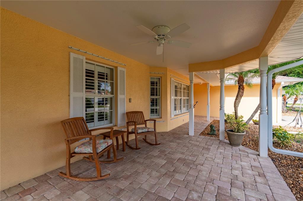 A covered patio features paver flooring, two wooden rocking chairs, and a ceiling fan — 23347 MULLINS AVENUE, PORT CHARLOTTE, FL