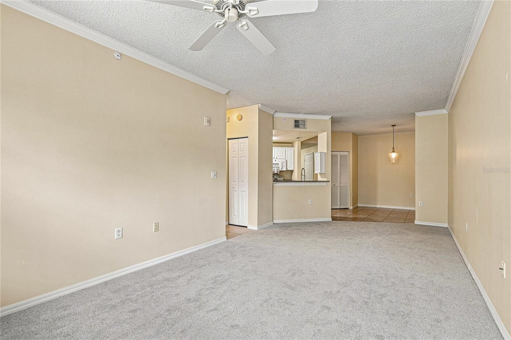 A living room with beige walls, gray carpeting, a ceiling fan, and an open kitchen — 5459 BENTGRASS DRIVE UNIT 2-110, SARASOTA, FL