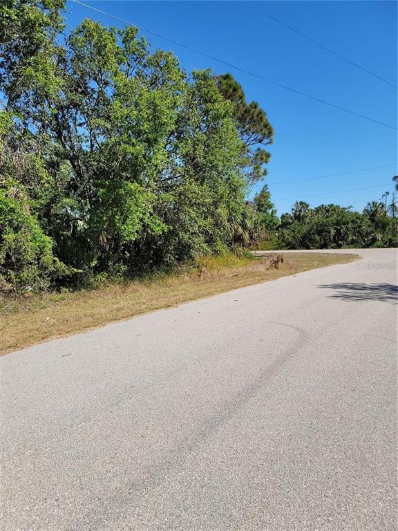 A paved road curves past a wooded lot under a clear blue sky — Lot 34 EASTMAN CIRCLE, NORTH PORT, FL