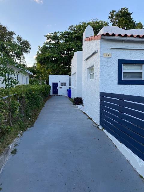 A concrete driveway leads between white stucco buildings toward a blue door in the distance — 55 NW 47th Street, Miami FL 33127, MIAMI, FL